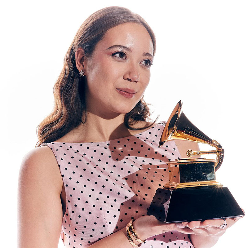 Laufey in a pink polka-dot gown holding a Grammy award.