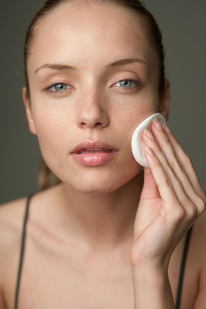 A woman applying skincare using a round cotton pad.